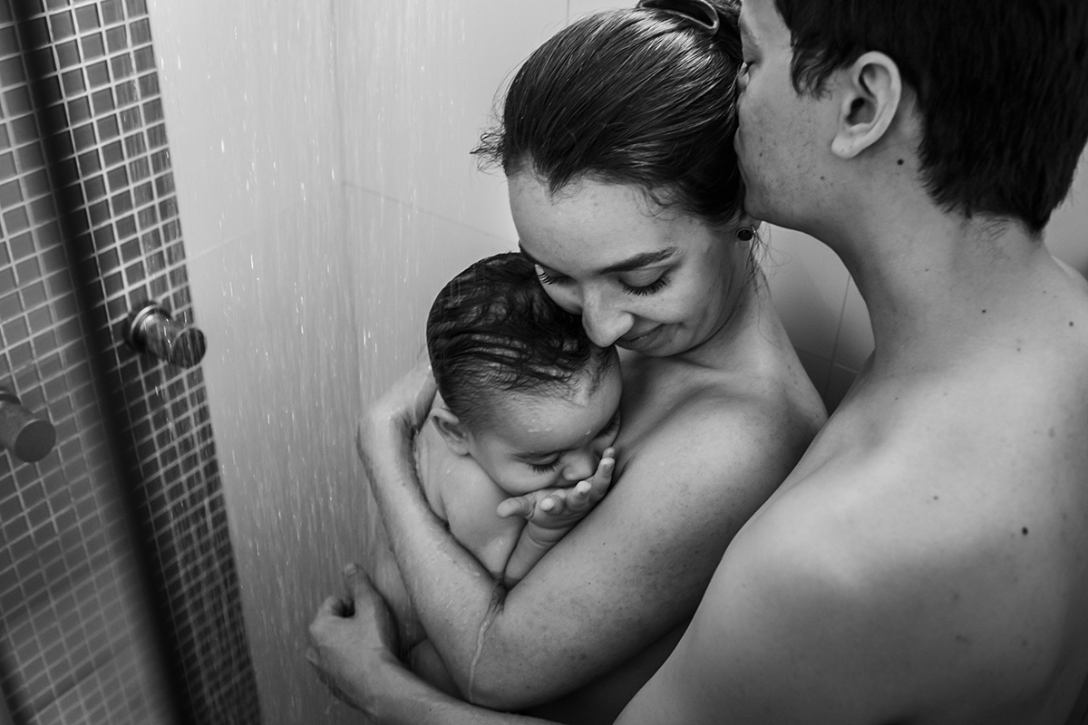 casal dando banho de chuveiro no seu bebê no colo