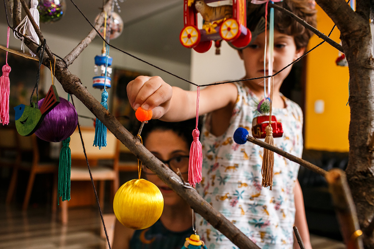 mãe ensina filho a enfeitar a árvore de natal com a colagem de bolinhas de feltro coloridas em foto de Adriana Costa