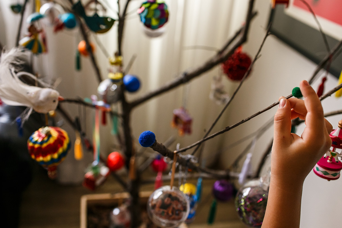 criança colando bolinhas de feltro colorida na árvore de natal