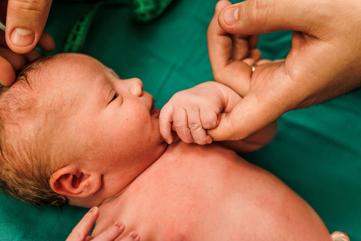 bebê tranquilo sob o carinho do pai durante os primeiros exames pós parto em foto de Adriana Costa