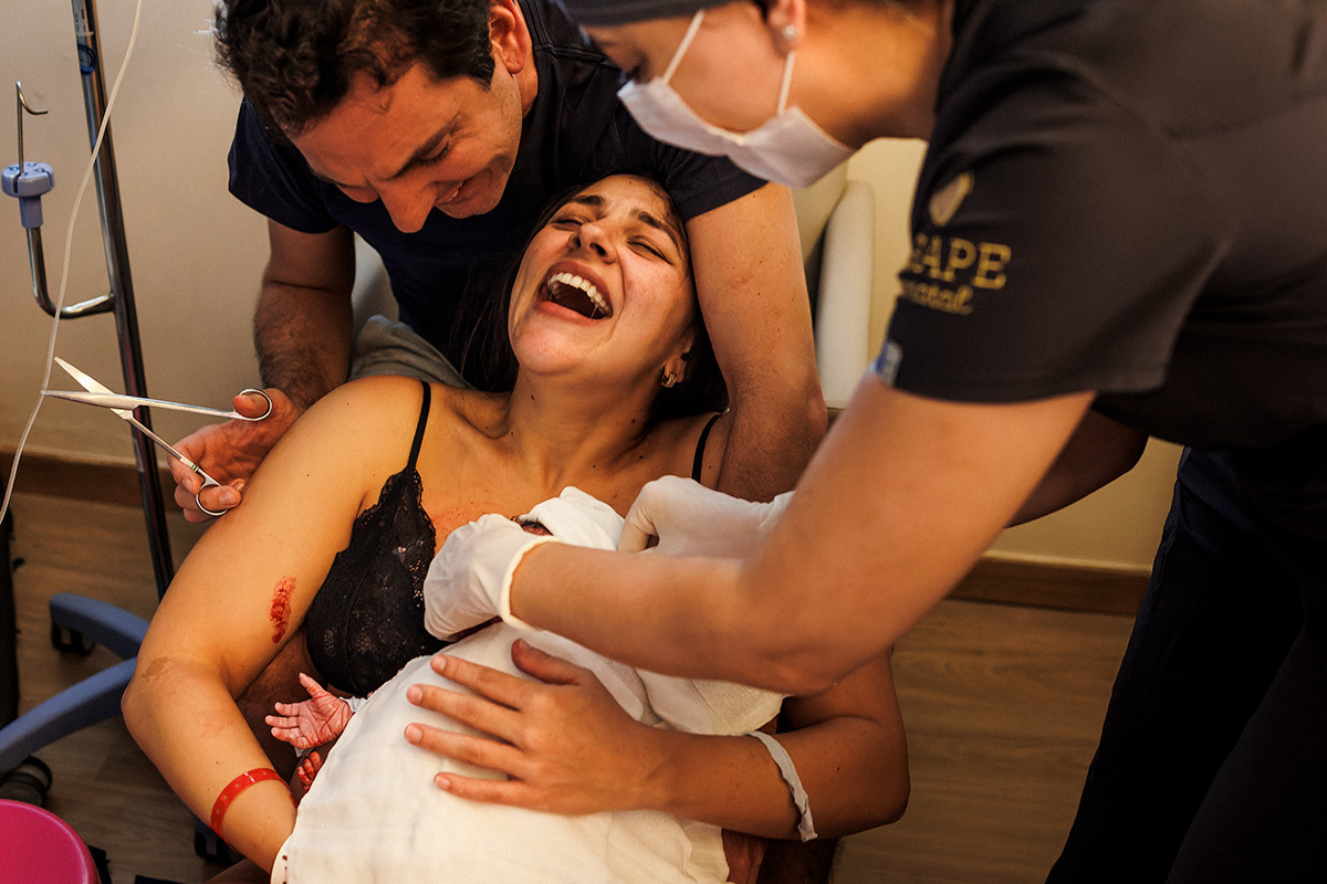 mulher não para de rir emocionada após o nascimento da filha em foto de Adriana Costa