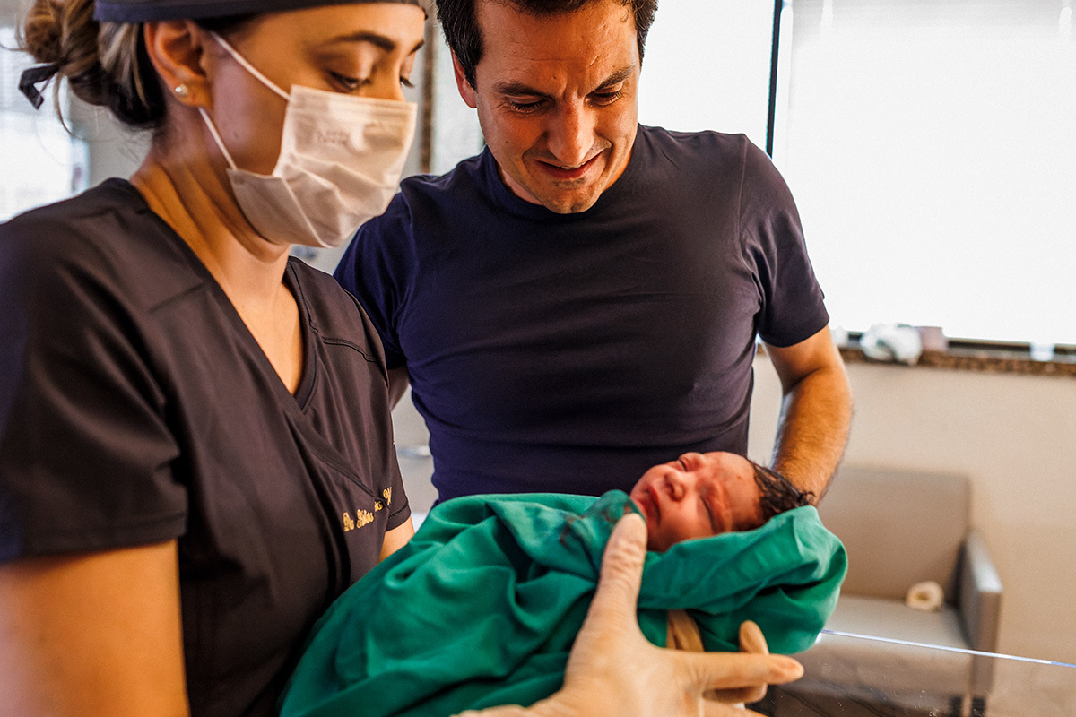 pai observa emocionado a pediatra cuidando da sua bebê