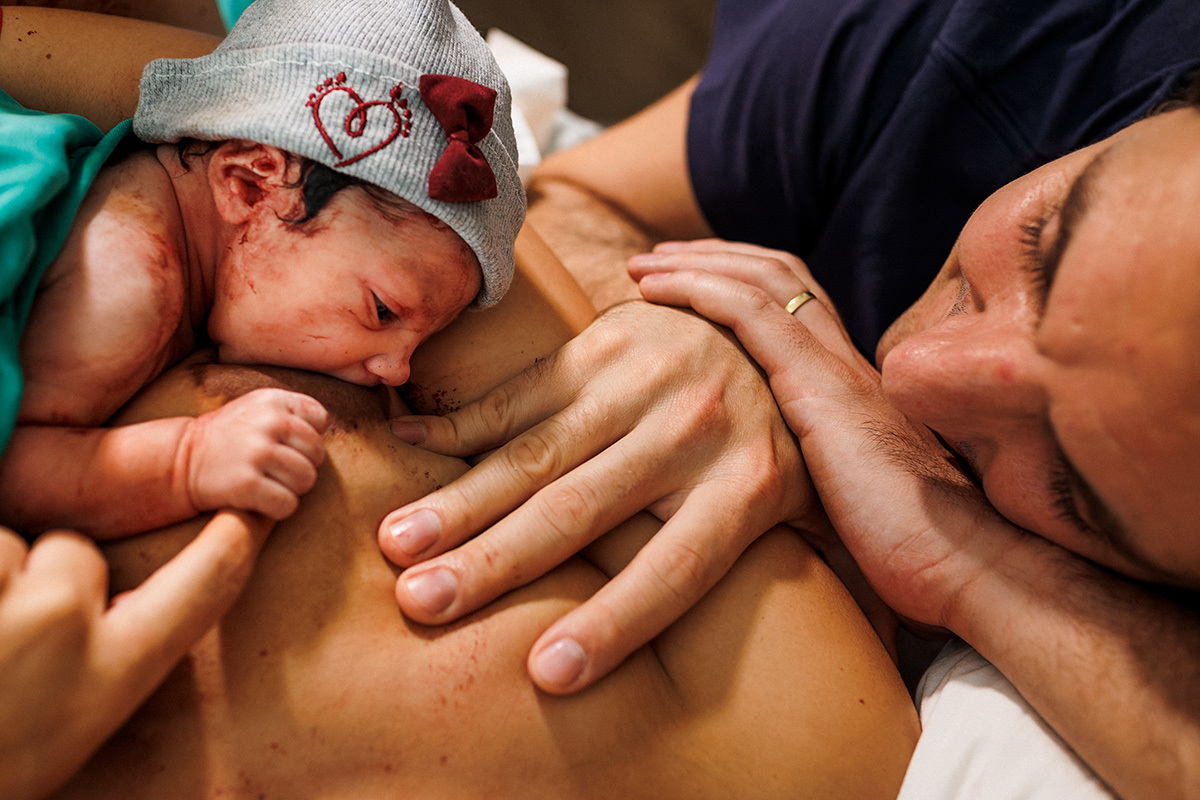 Foto de Adriana costa do pai observando sua filha realizar a primeira amamentação após o parto