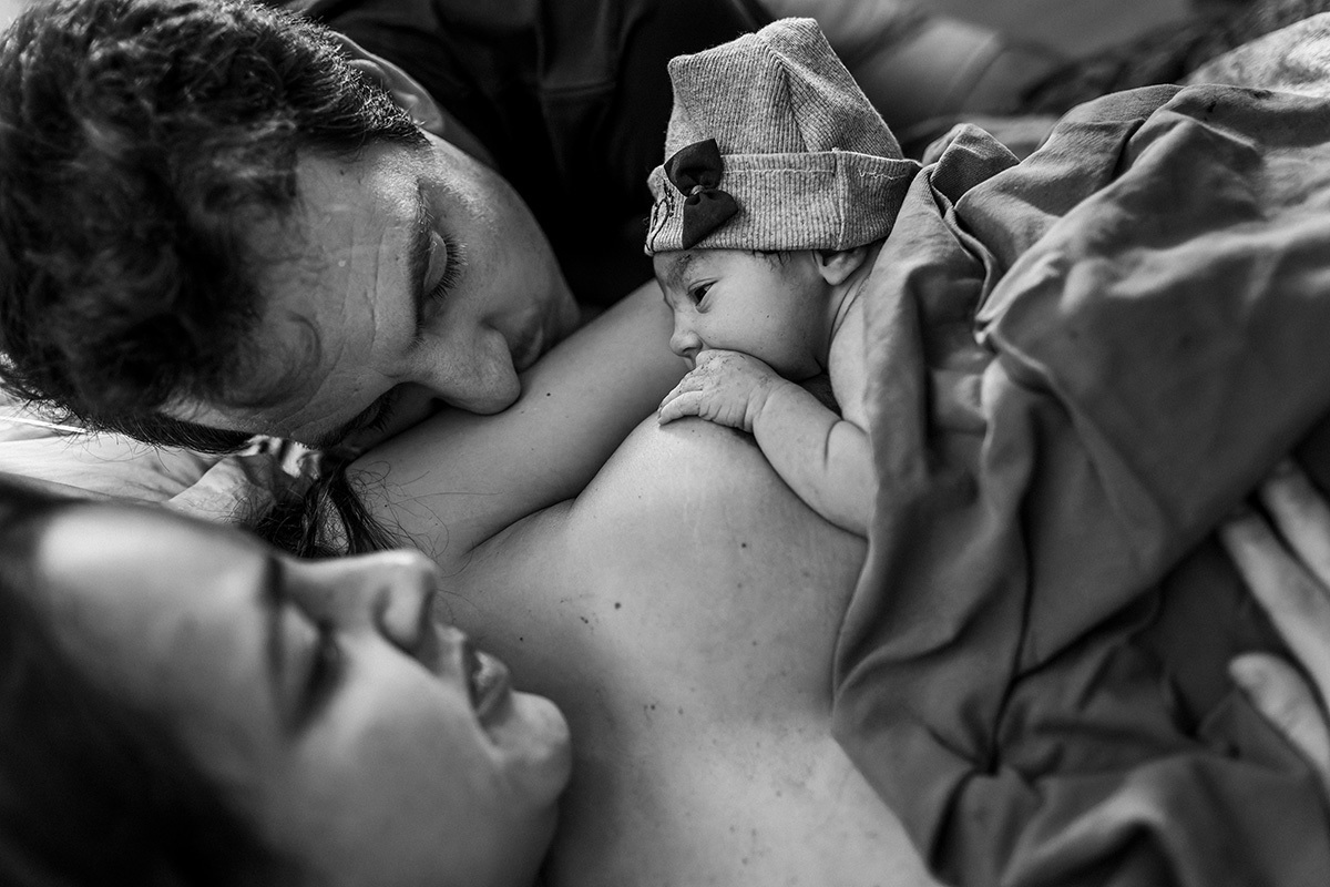 pais observam carinhosamente sua filha amamentando durante a hora de ouro