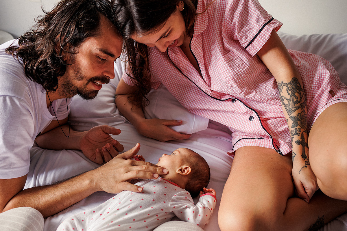 pais em casa com seu bebê recém-nascido em foto de Adriana Costa