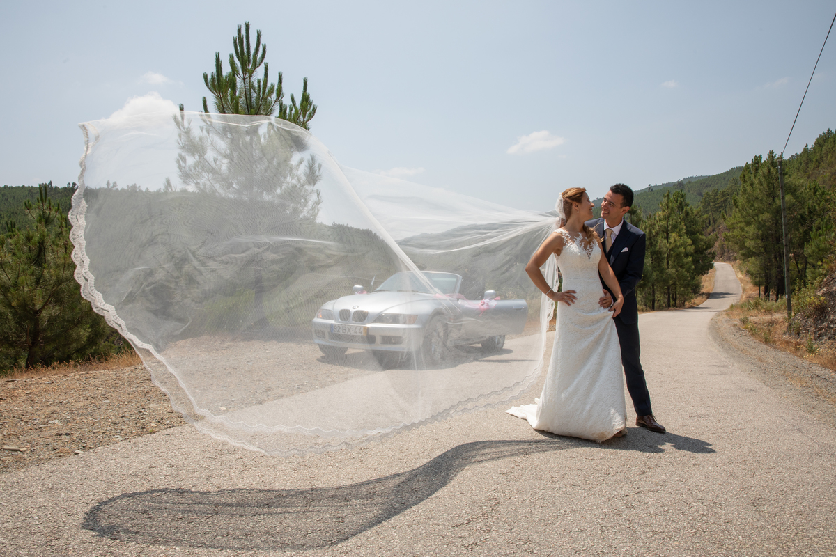 O véu da noiva, os noivos e o seu carro em paisagem de estrada