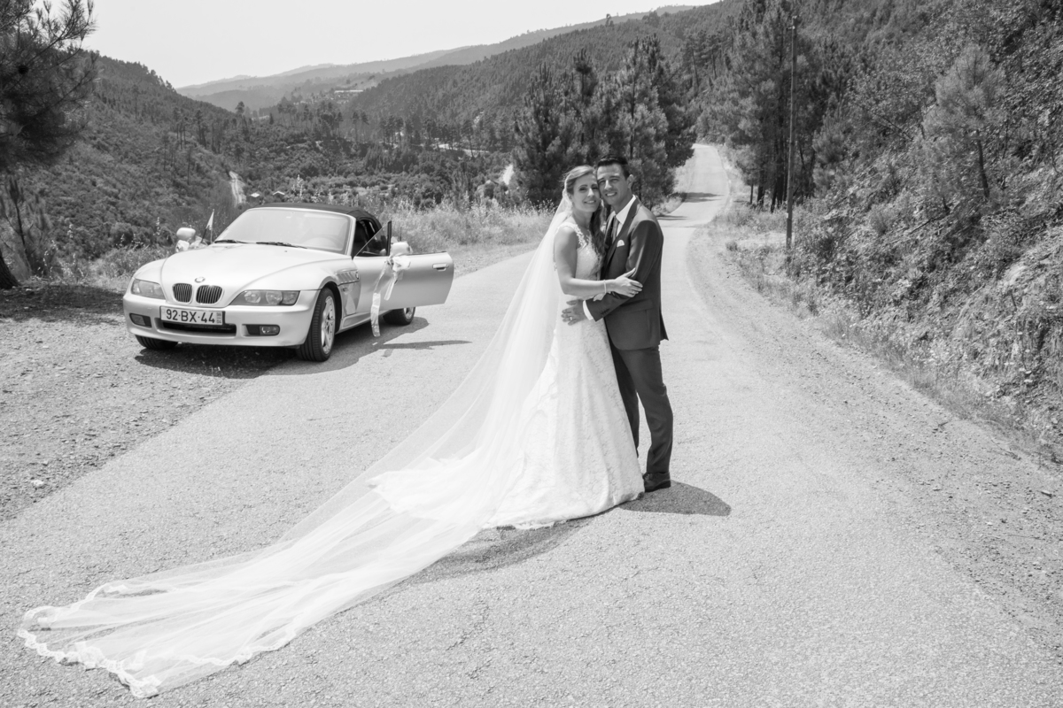 O véu da noiva, os noivos e o seu carro em paisagem de estrada a preto e branco