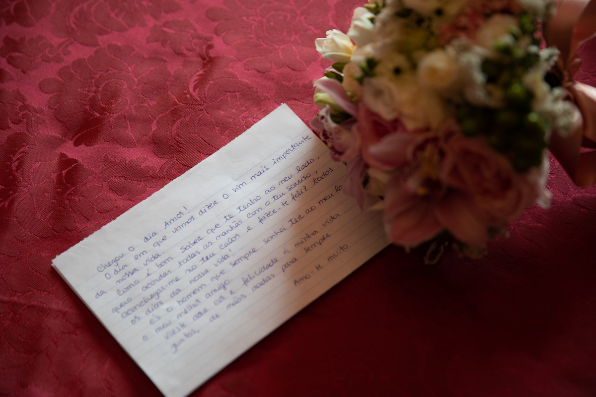 Carta com mensagem do noivo e buque da noiva ao lado sob fundo vermelho