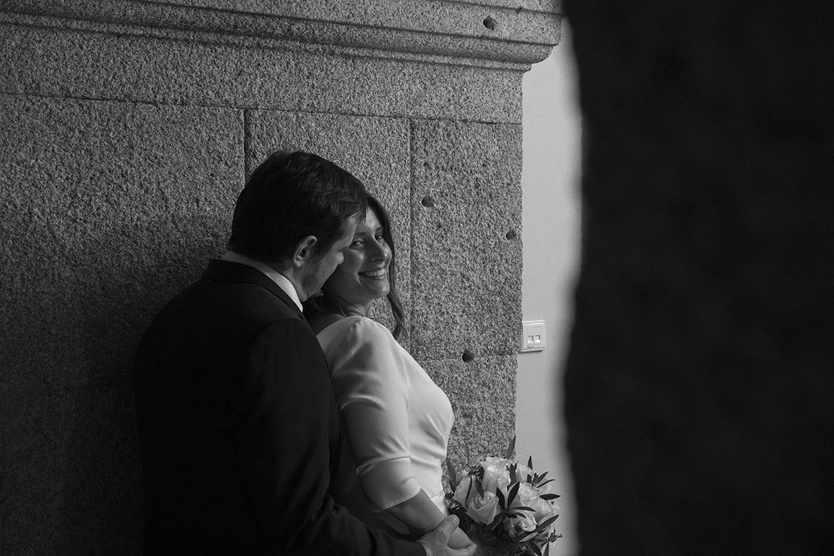 Num registo a preto e branco, Nuno abraça Rita por trás, observando-a com ternura. Ela sorri amplamente, olhando para o lado.