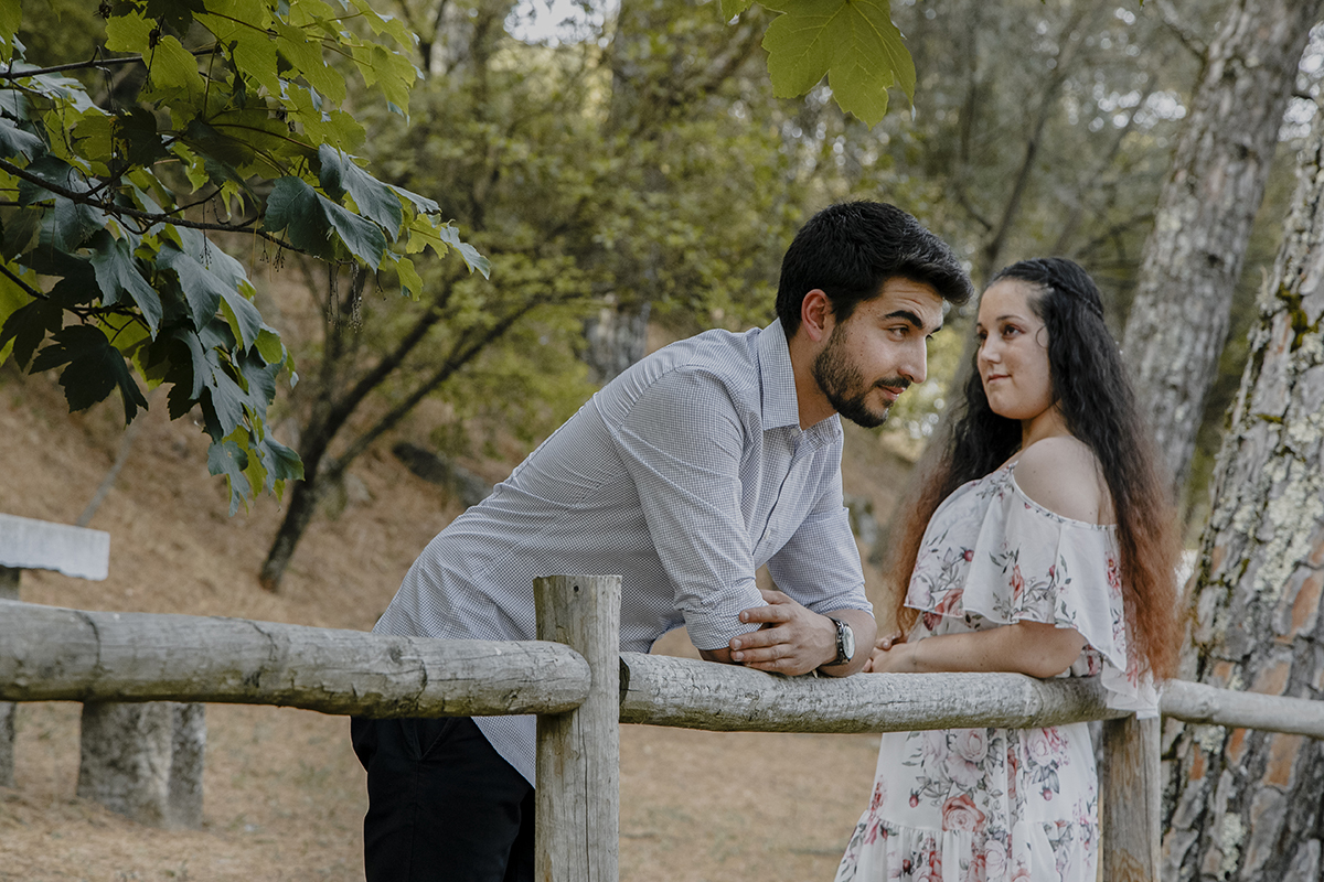Encostados a um corrimão de madeira, Miguel e Juliana partilham um momento de introspeção, os seus olhares sérios reforçam a profundidade do que sentem.