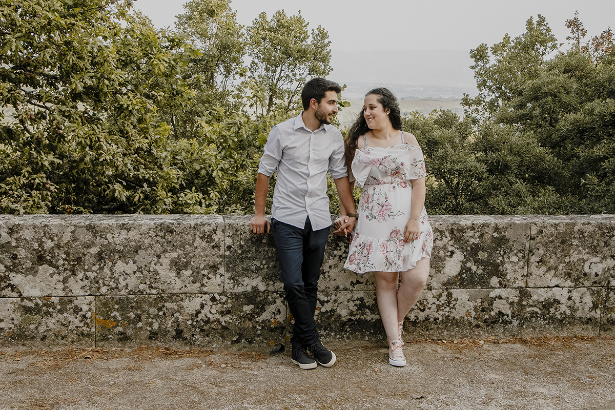 De mãos dadas e lado a lado, entre ramos verdes, o amor entre eles é palpável, irradiando felicidade e cumplicidade perante a natureza que os rodeia.