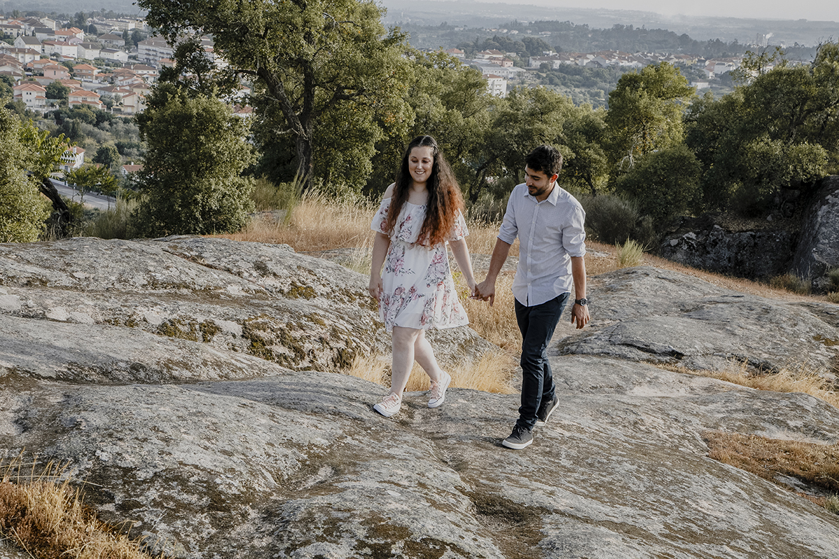 Caminhando juntos sobre as rochas, olham para baixo com sorrisos felizes, partilhando cada passo e cada instante.