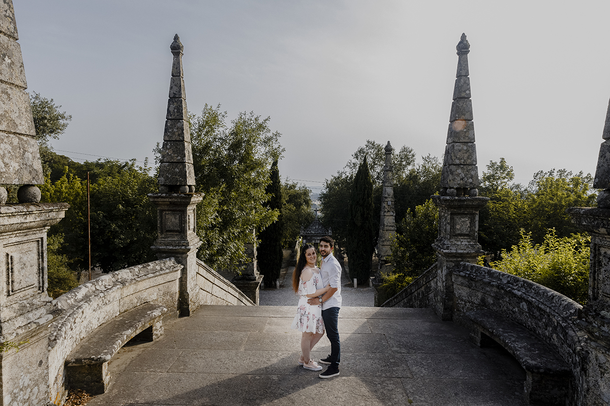 De corpo inteiro e lado a lado, abraçados e de frente para a câmara, mostram a força do seu vínculo, com a escadaria e a paisagem verde ao fundo.