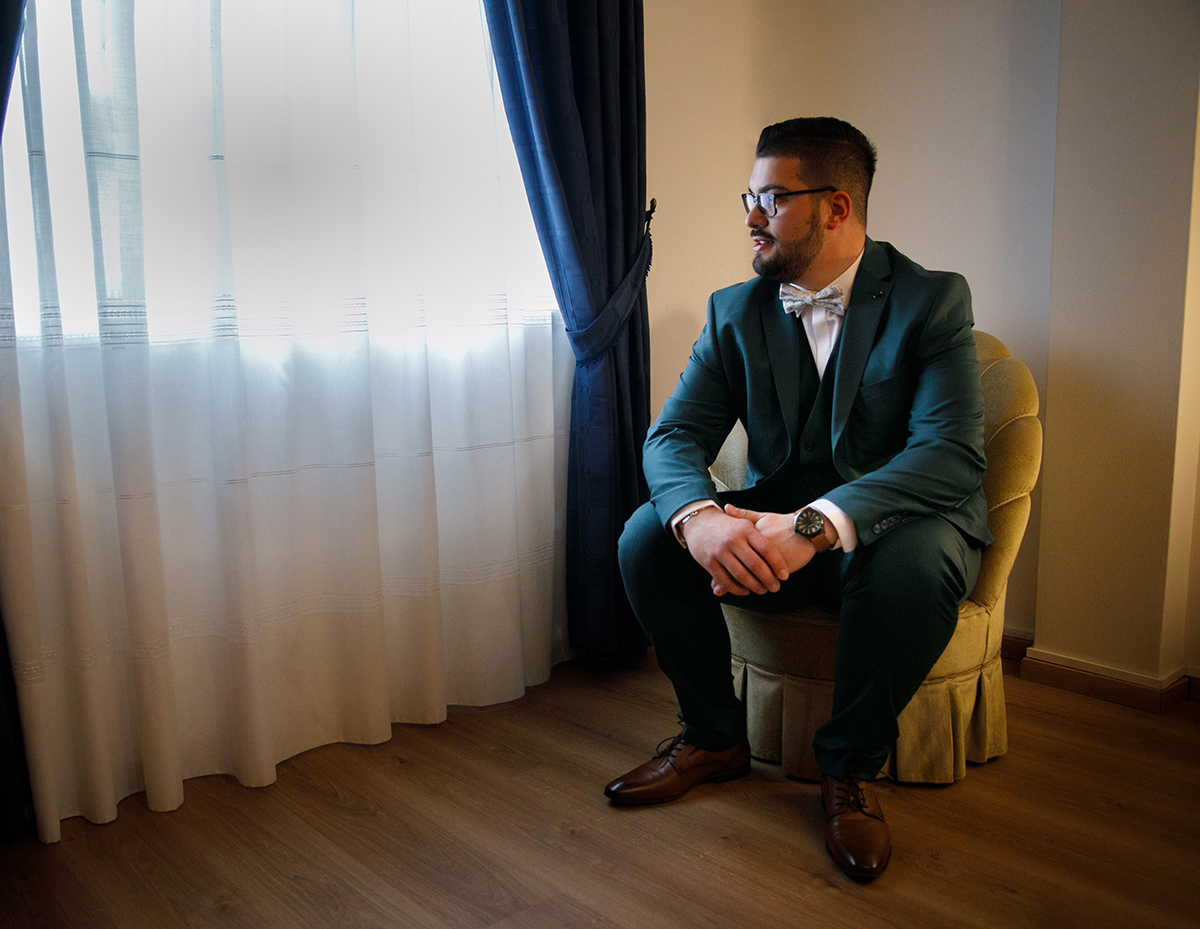 Tiago, sentado perto da janela, contempla a luz que lhe acaricia o rosto, as mãos tranquilamente entrelaçadas sobre os joelhos, num instante de introspeção feliz que captura a serenidade do seu espírito naquele dia especial.