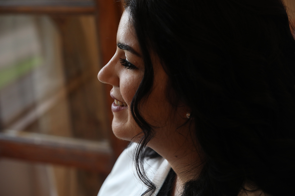 De perfil e iluminada pela luz suave da janela, Carolina sorri com naturalidade, o rosto radiante e cheio de esperança, enquanto o mundo lá fora parece suspenso em admiração.