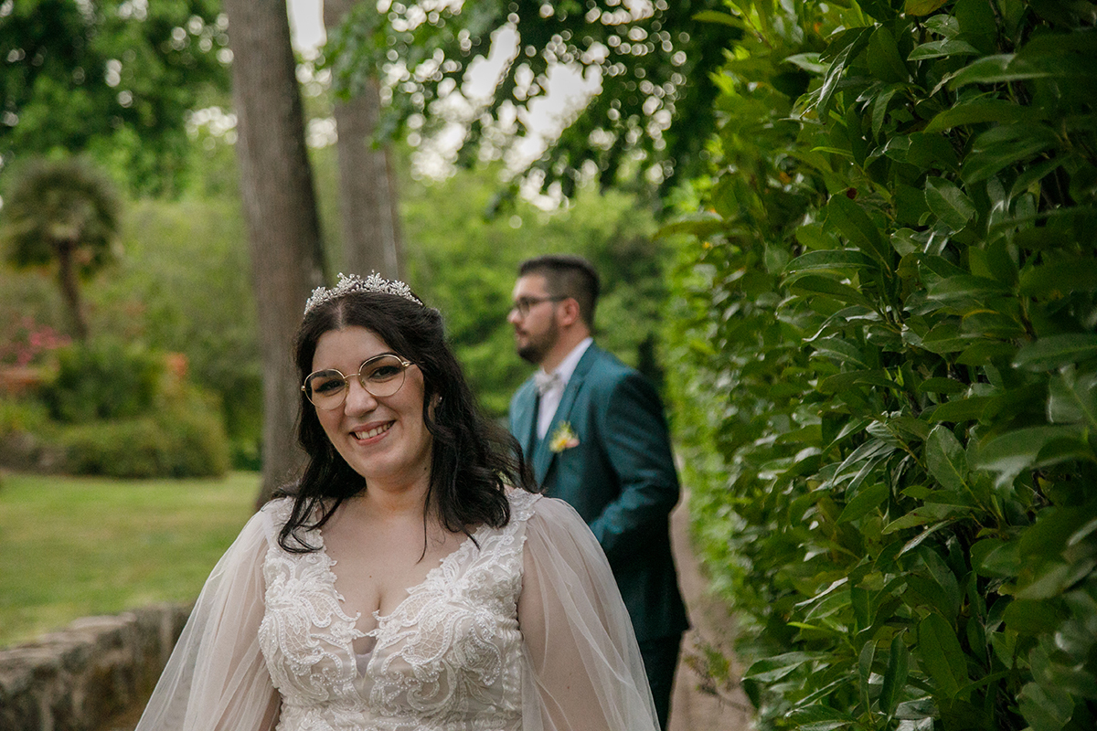 Um plano mais próximo revela o sorriso radiante de Carolina enquanto a sua tiara brilha com delicadeza, Tiago aparece ao fundo, ligeiramente desfocado, contemplando-a com admiração, um retrato de amor que fala sem palavras.