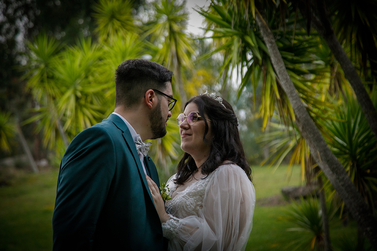 Frente a frente e captados num plano com vinheta, eles trocam olhares apaixonados e sorrisos genuínos, Carolina pousa a mão no peito de Tiago e por trás um jardim tropical de palmeiras cria um cenário de conto de fadas moderno.