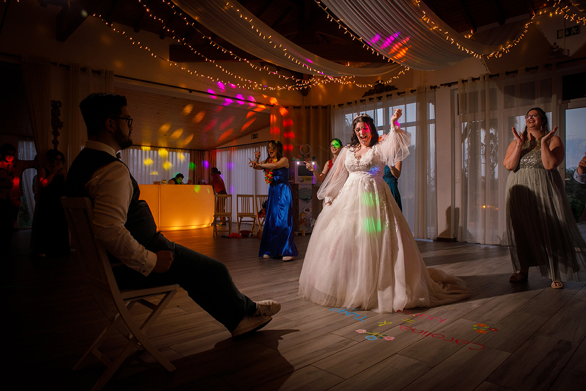 Com um caleidoscópio de cores a preencher o espaço, Carolina dança no centro da pista com uma energia contagiante, enquanto Tiago, sentado, admira a sua alegria, e amigas da noiva acompanham a festa numa celebração cheia de vida.