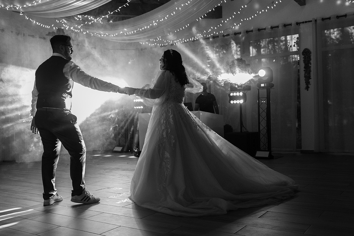 A preto e branco, na pista de dança, Tiago estende a mão a Carolina num gesto convidativo e carinhoso, ela sorri e aceita com o vestido a esvoaçar, captando um momento cheio de elegância, amor e movimento harmonioso.