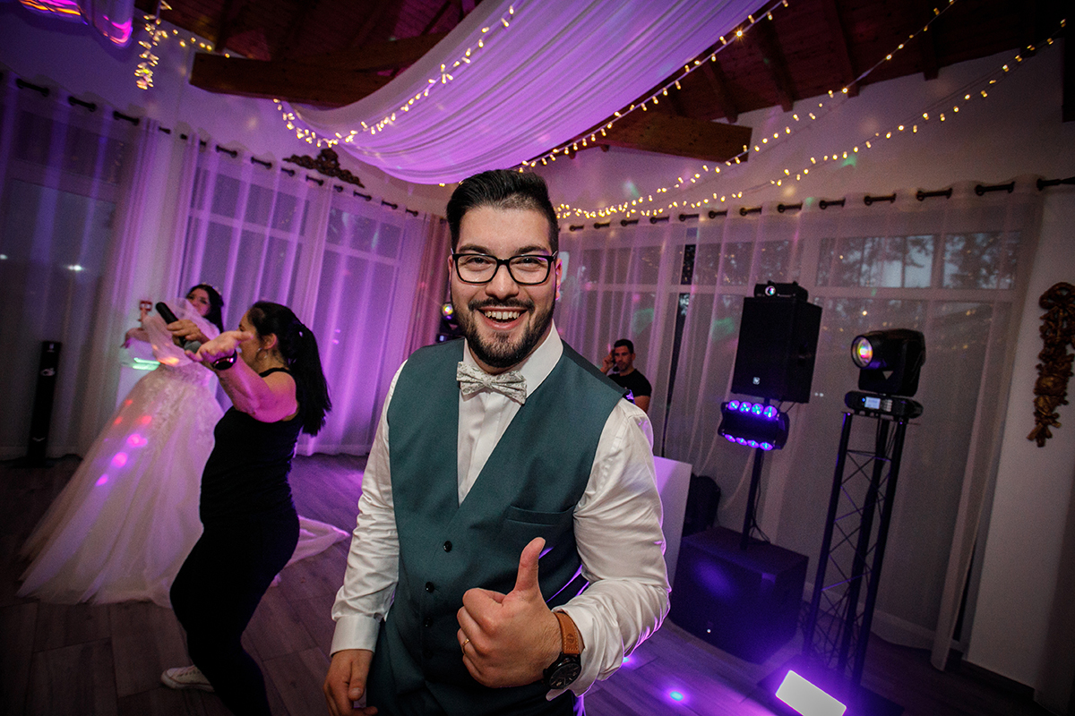 Sob uma luz roxa vibrante, Tiago destaca-se no meio da pista sorridente e a fazer um gesto descontraído com a mão, enquanto os convidados ao fundo se perdem na dança e na alegria de celebrar a união.