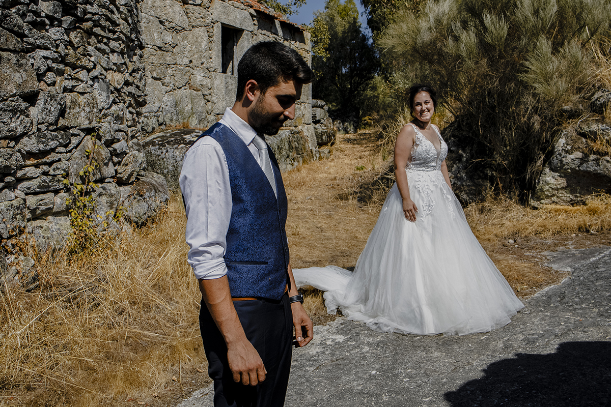 Num plano mais afastado, Miguel aparece dos joelhos para cima, olhos fechados em reflexão, enquanto Juliana, de corpo inteiro, sorri levemente para ele, ambos no mesmo cenário sereno.