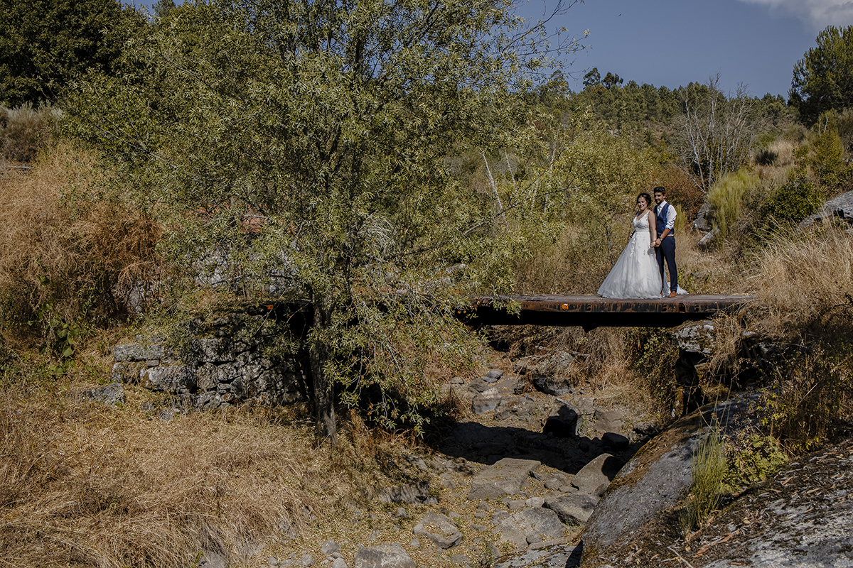 Num plano muito afastado, o casal está no topo de uma ponte, Miguel atrás segurando as mãos de Juliana, ambos olhando para a câmara com expressões de felicidade.