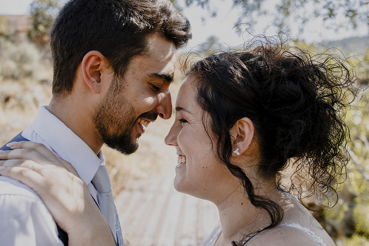Dos ombros para cima, frente a frente, Juliana mantém a mão no ombro de Miguel, rostos próximos, olhos fechados e sorrisos suaves, capturando um momento íntimo.