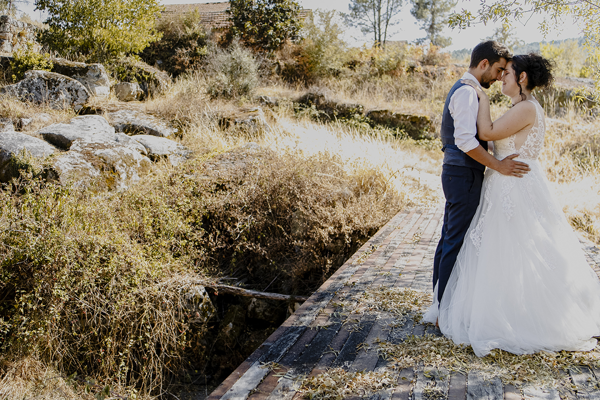 À direita da imagem, de corpo inteiro, Miguel abraça Juliana pela cintura enquanto ela coloca as mãos nos seus ombros. Com os olhos fechados, tocam os narizes, rodeados por rochas e ervas.