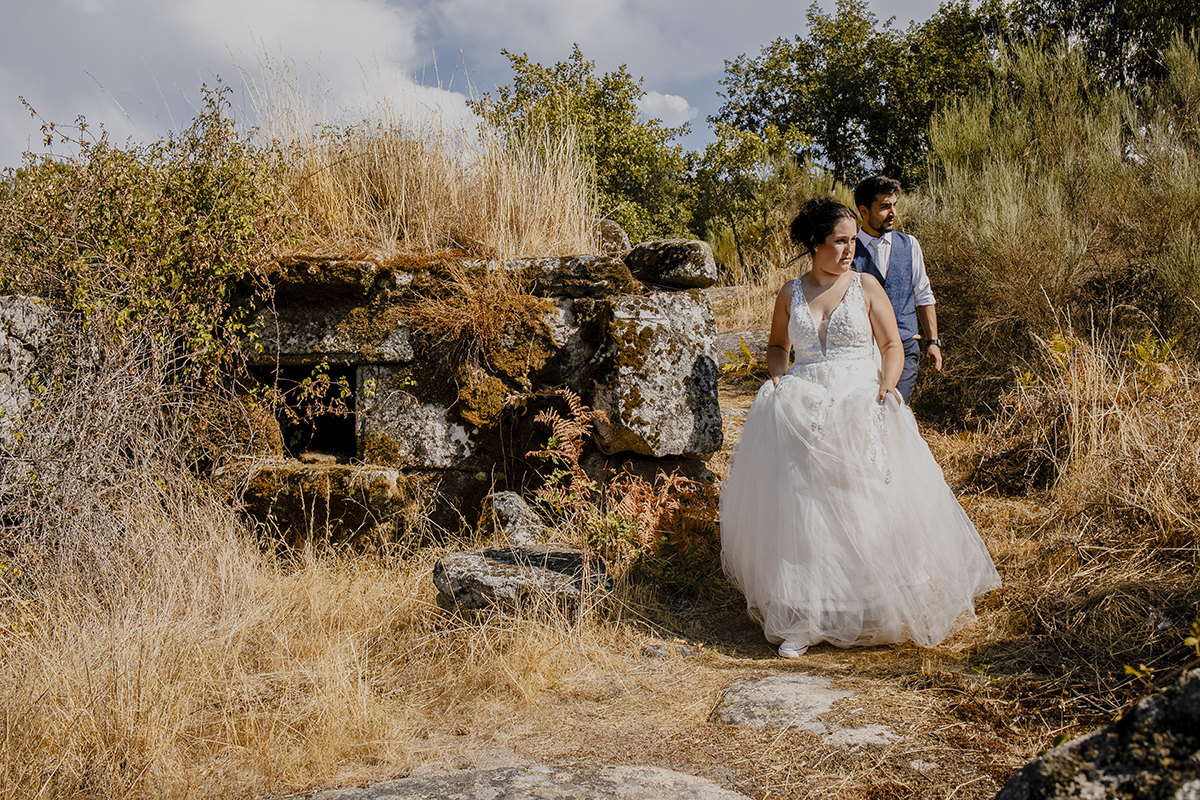 No mesmo cenário, agora ao pé do muro antigo de pedra, de frente para a câmara, mas olhando para o lado com expressões sérias, refletindo momentos de introspecção.