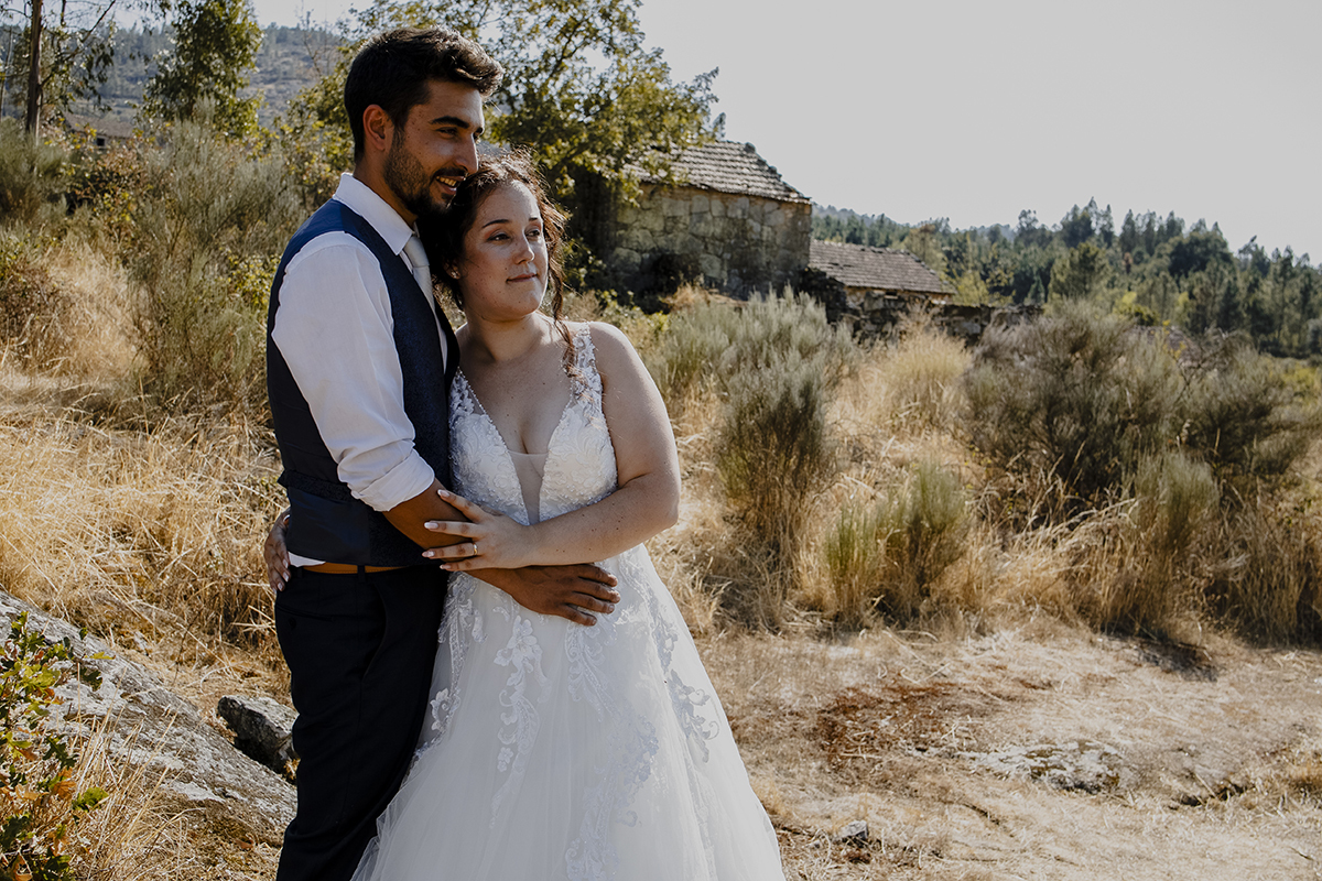 Aqui vemos os dois do lado esquerdo da foto, dos joelhos para cima, os dois estão lado a lado abraçados a olharem para a frente a sorrirem.