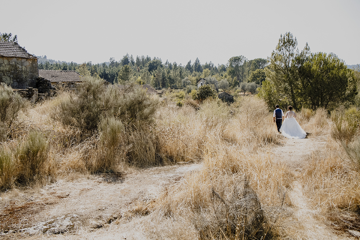 Aqui vemos os dois em um plano mais afastado e os dois estão de costas e caminham de mãos dadas, num cenário de ervas castanhas e algumas verdes e construções antigas ao fundo.