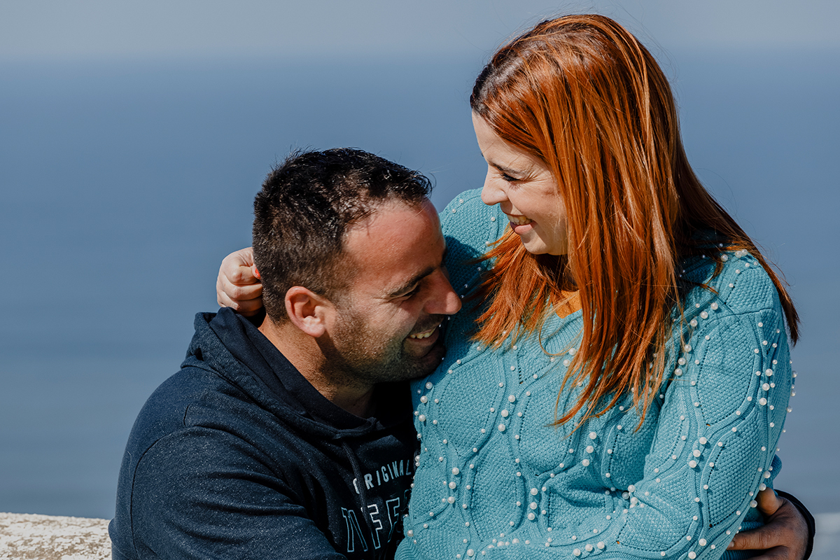 Num gesto divertido e apaixonado, Mónica senta-se sobre Ricardo. Os risos explodem e os braços envolvem-se num abraço caloroso. Um instante leve e inesquecível.