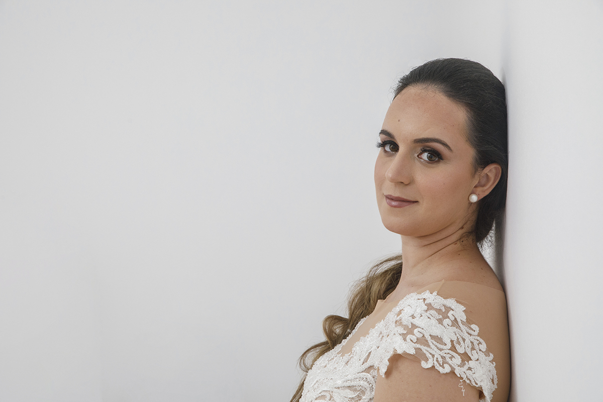 Encostada a uma parede branca, Marta aparece de lado, séria e feliz, a olhar diretamente para a câmara, como quem se revela com firmeza e doçura ao mesmo tempo.