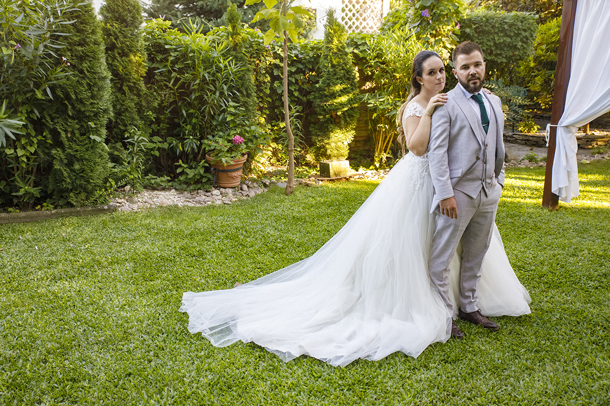 Descrição: Aqui estão em um jardim e a Marta está atrás colocando as mãos sobre os ombros de Ricardo que está á sua frente e os dois olham sérios e felizes para a câmara e o vestido da Marta percorre o relvado.