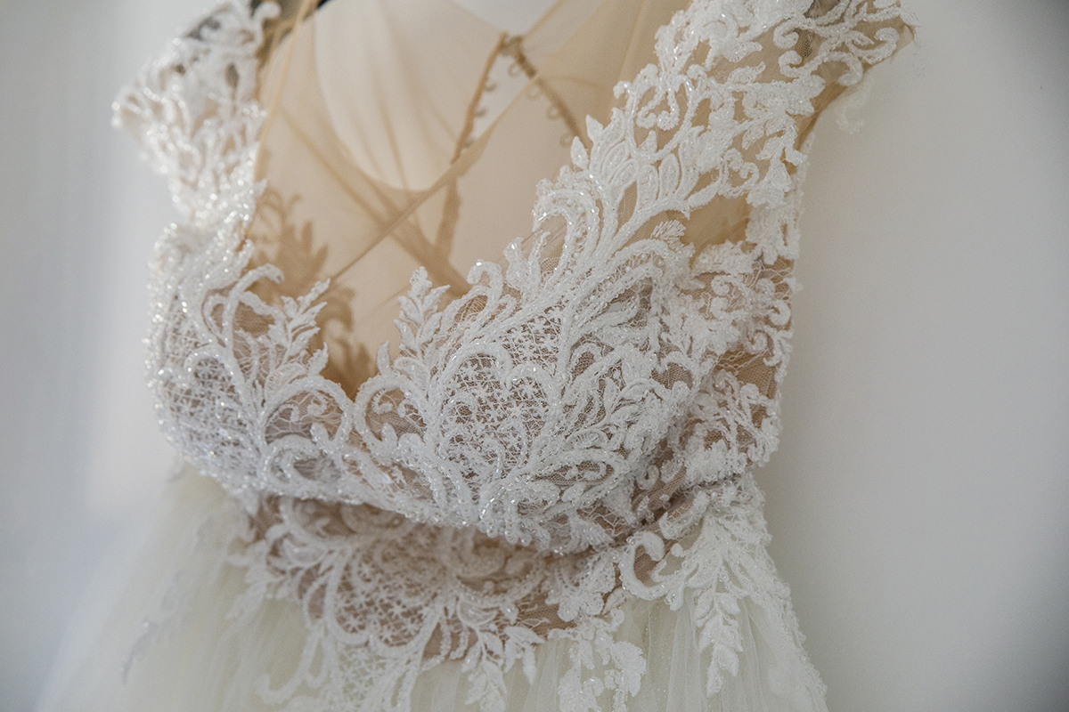 Num plano de detalhe delicado, o vestido surge do peito até aos ombros com os seus detalhes rendados em evidência, branquinho e etéreo, como uma promessa de pureza e encanto.