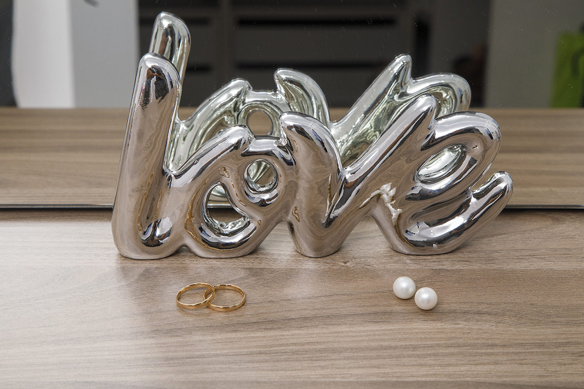 13. Entre reflexos e ternura, um espelho ao fundo e uma plaquinha prateada a dizer love acompanham as alianças e os brincos dispostos com cuidado, num pequeno altar de significados.