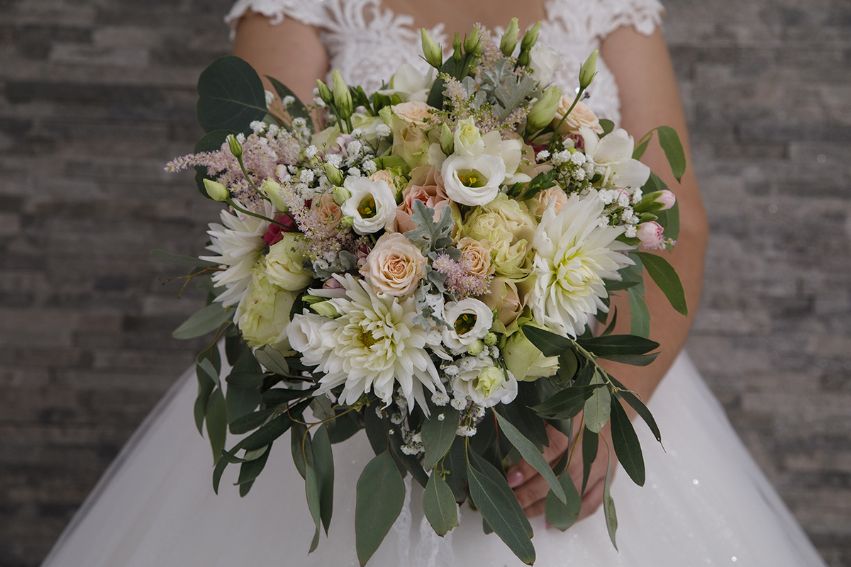 Em foco vemos o bouquet da noiva inclinado suavemente na direção da lente, com as flores em tons de verde, branco, rosa e amarelo a destacarem-se como pinceladas de vida e atrás dela desfocada, quase como um sussurro, está Marta, serena como uma pintura.