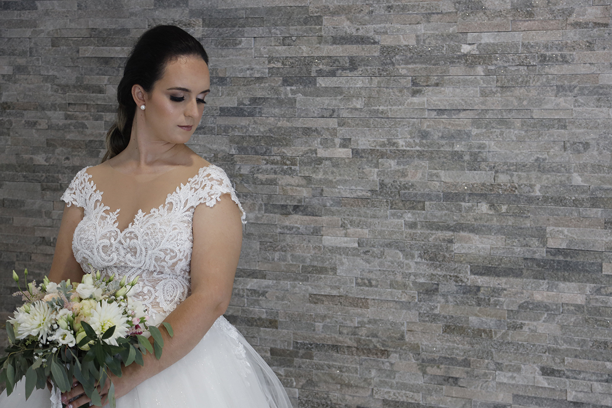 Num fundo em tons suaves de cinzento e castanho claro, Marta aparece do lado esquerdo da imagem com o bouquet pousado delicadamente à sua frente, a olhar para baixo com uma expressão que mistura serenidade e contemplação.