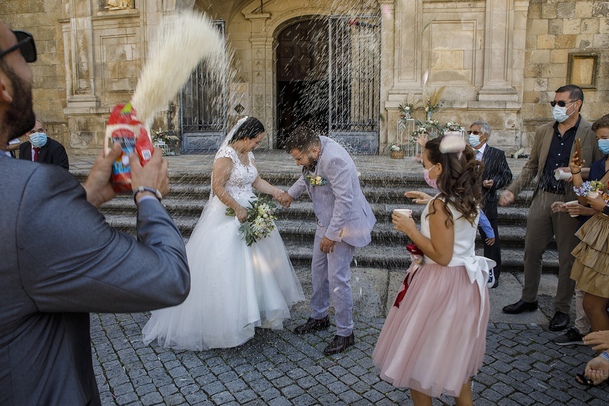 Já cá fora, os convidados atiram arroz com alegria enquanto os noivos, de mãos dadas e cabeças levemente baixas, atravessam a chuva de votos e sorrisos sem nunca se largarem.