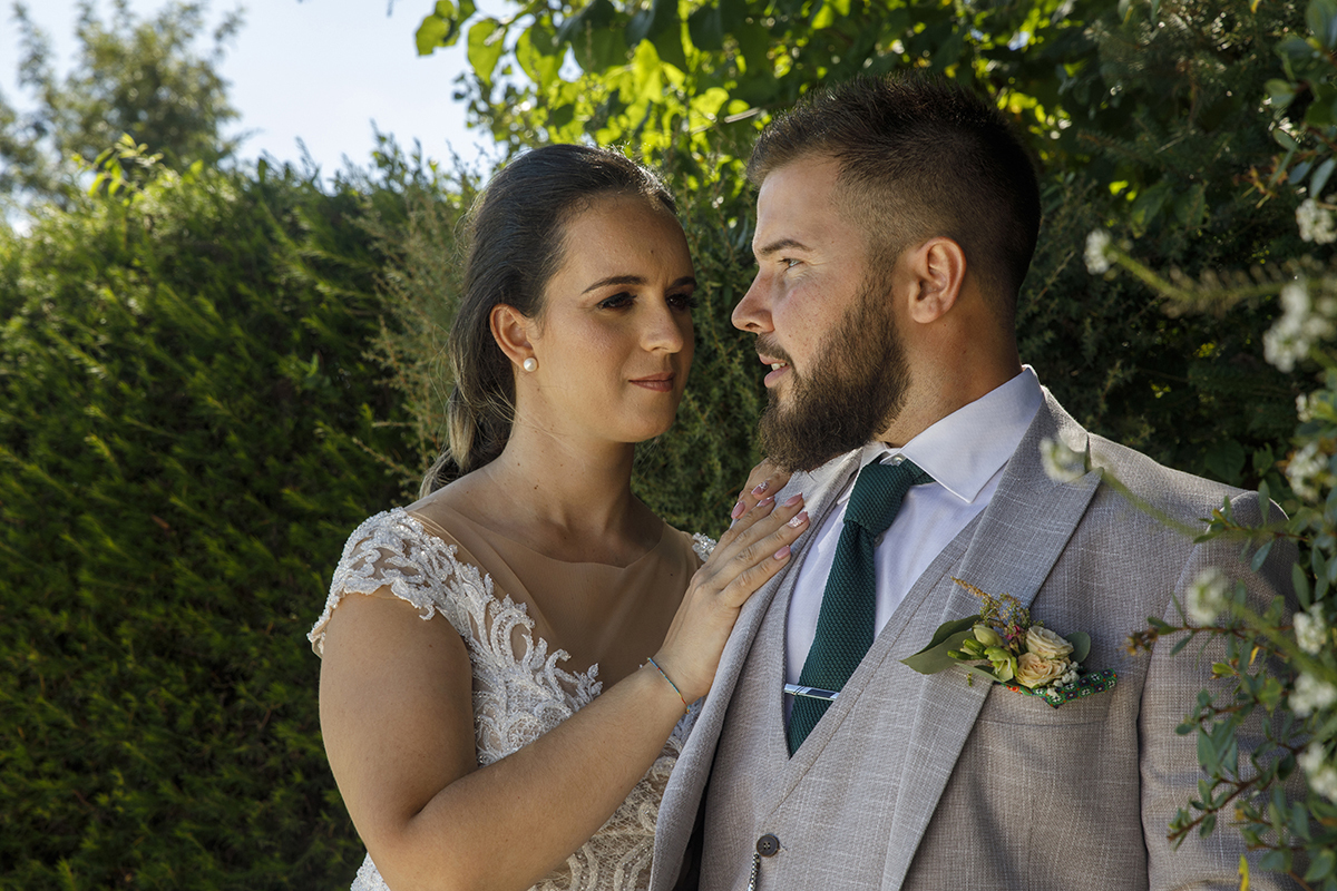 Descrição: Aqui vemos os dois com um cenário verde de arbustos por trás e os dois estão lado a lado e ela coloca a sua mão no peito dele e olha para ele seriamente feliz e reflexiva e olha para frente.