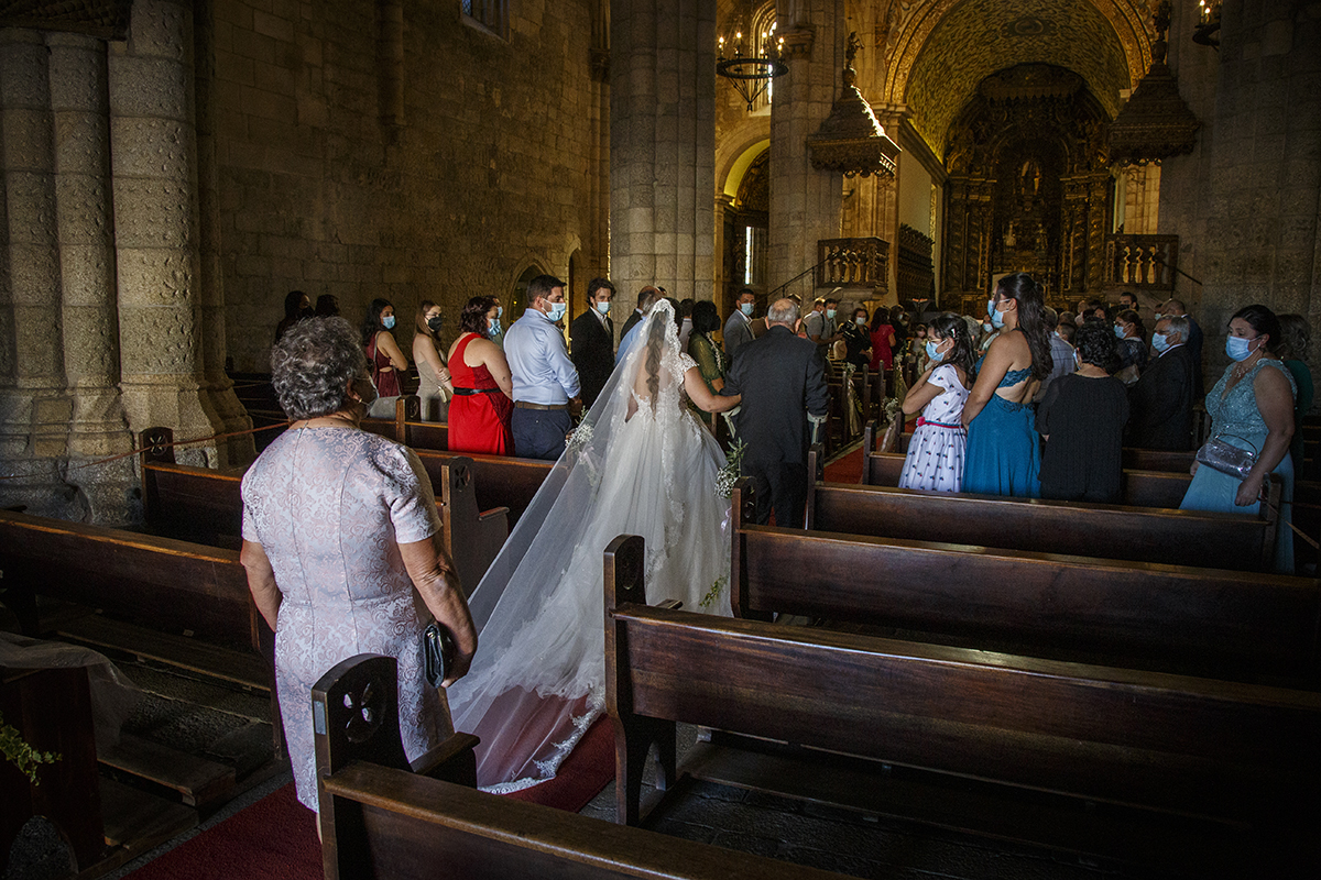 Já no interior da Sé, vemos a entrada solene da noiva com o braço dado ao pai, caminhando pelo corredor central enquanto os convidados se levantam e observam com emoção aquele momento cheio de significado.