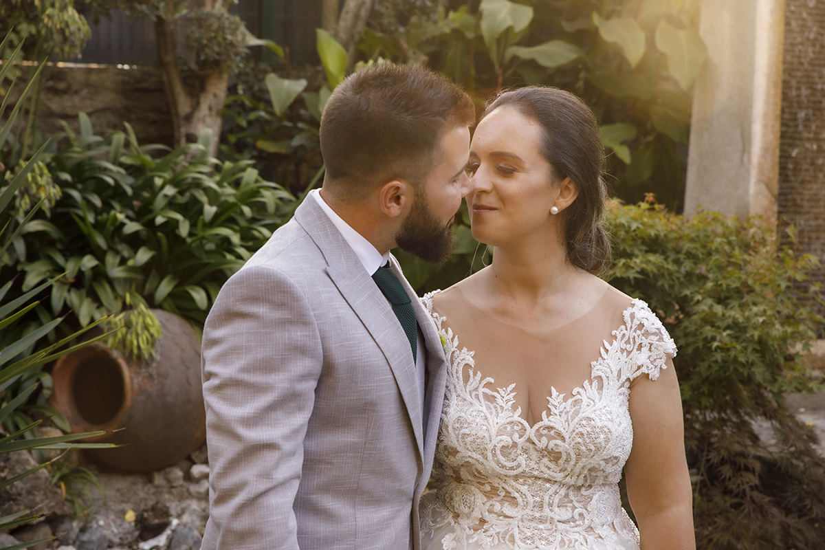 Descrição: Aqui vemos no cenário do jardim com pedras e vasos e plantas os dois da cintura para cima, os dois encaram-se e quase se beijam e estão de olhos fechados.