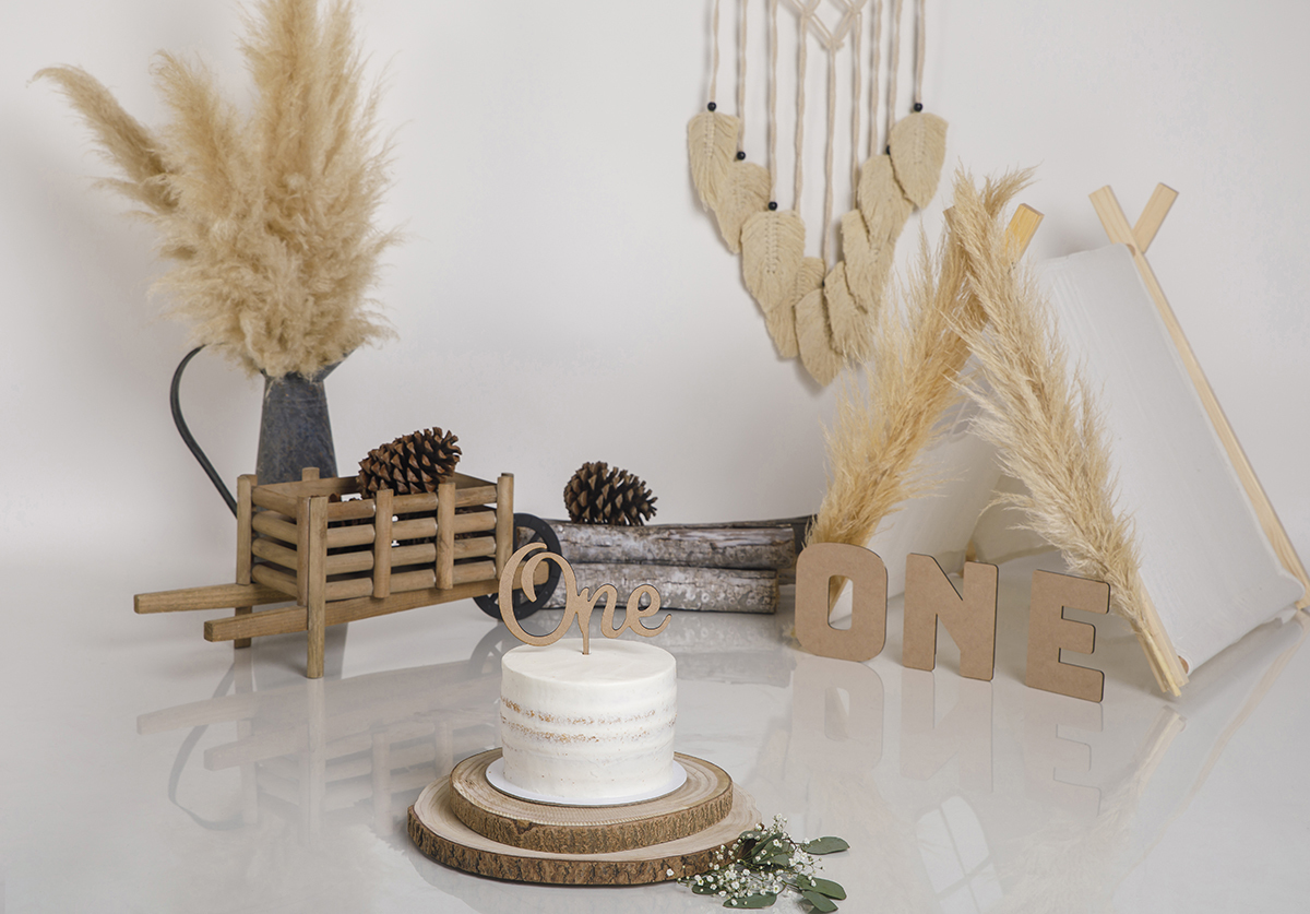 O cenário perfeito para o grande momento: o bolo branco do Daniel está impecável, em cima de tábuas de cortiça com o topper “ONE”. Um convite para a festa começar.