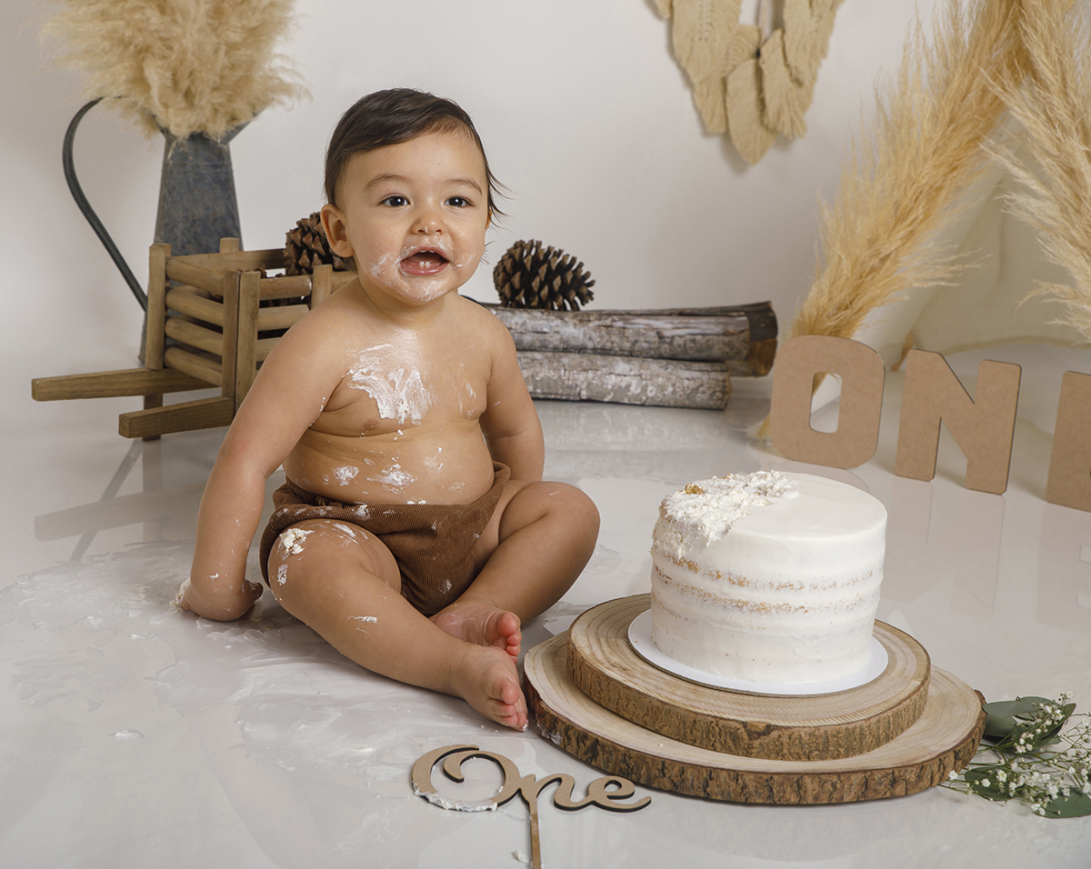 Sentado ao pé do bolo, de boca aberta e olhar decidido, Daniel está cheio de bolo por todo o lado. O seu fato castanho já conta uma história de festa que correu muito bem!
