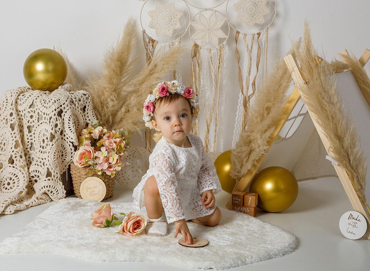 Num cenário encantador, dois ramos adornados com delicadas plantas em forma de penas formam um 'V' invertido, emoldurando a pequena Constança. Sentada ao centro, ela olha para a câmara de Foto Coimbra.