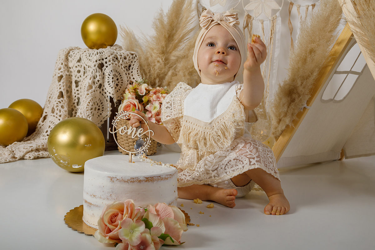 Coberta de creme e com a mão cheia de bolo esticada para cima, a Constança olha para o alto com a boca cheia, uma celebração doce e divertida.
