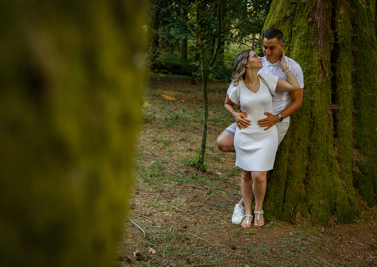 Com um tronco desfocado do lado esquerdo e outro tronco ao fundo, Jorge e Sabrina partilham mais um momento de ternura. Jorge está atrás com as mãos na cintura de Sabrina, enquanto ela segura com uma mão a mão dele sobre a sua barriga.