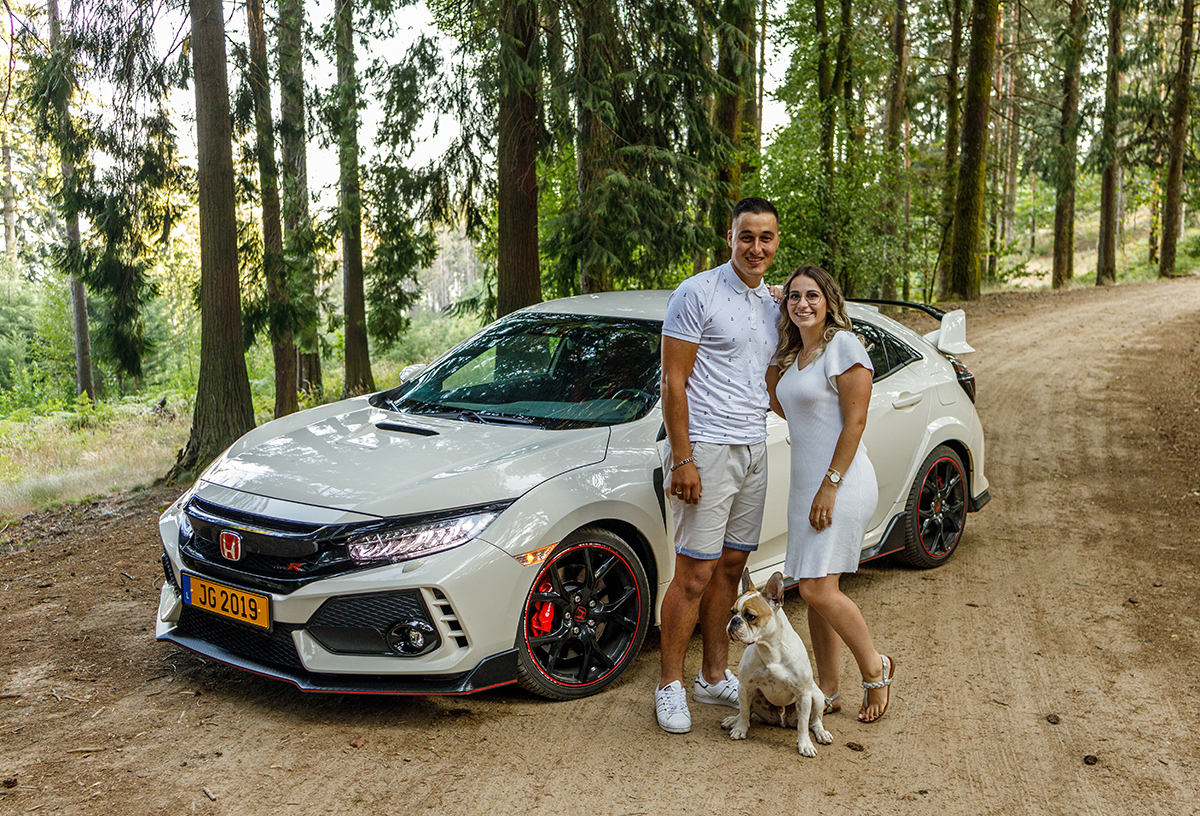 Num caminho de terra batida, os dois apaixonados estão lado a lado, encostados ao seu carro, muito felizes. À sua frente, o cãopanheiro aparece sério e atento, olhando para o lado.