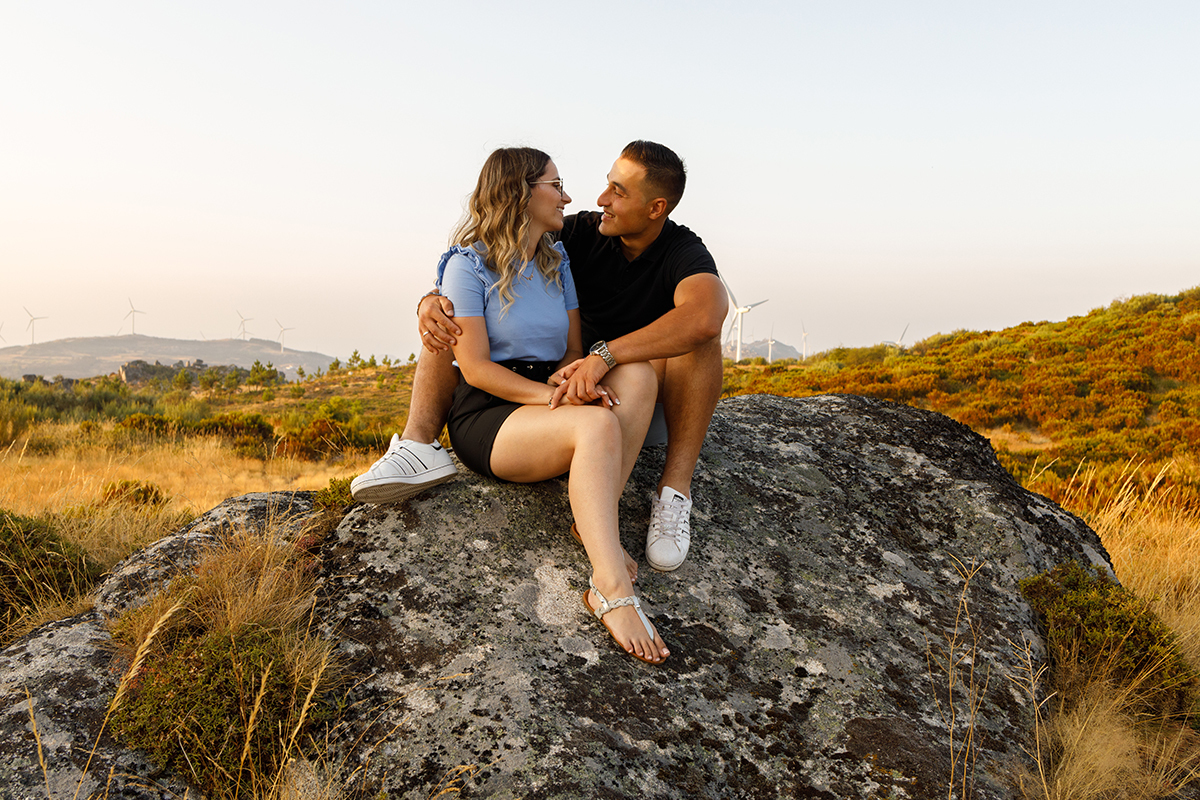 Sobre uma rocha, os dois sentam-se de frente um para o outro. Jorge segura as mãos de Sabrina e apoia uma mão nas suas costas. Os dois sorriem, rendidos ao momento.