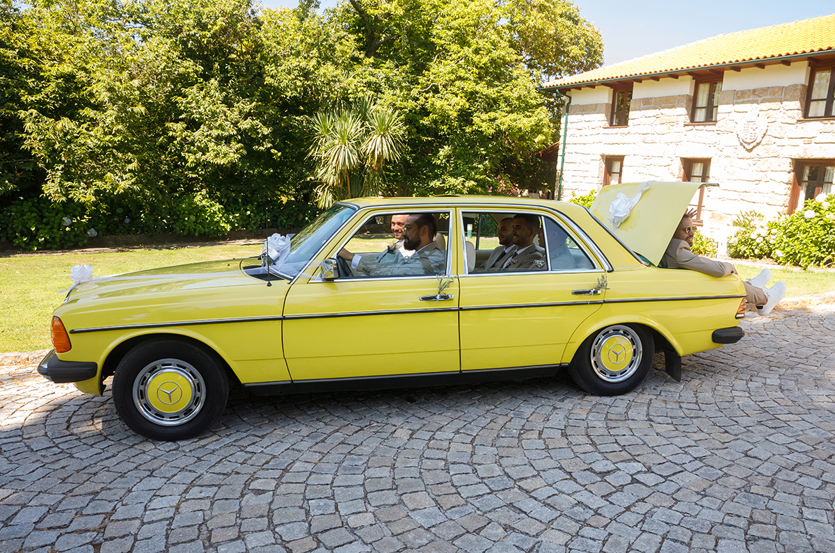 Um clássico Mercedes-Benz 200 amarelo dos anos 70 brilha com charme vintage. O noivo e os amigos enchem o carro de gargalhadas, até mesmo a mala se junta à festa.